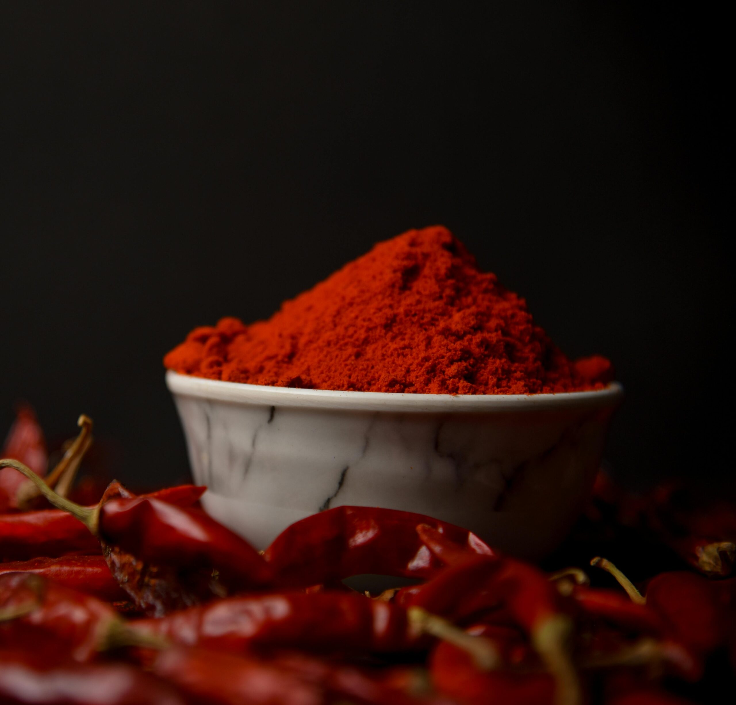 pexels photo 33440709 33440709 A bowl of vibrant red chili powder surrounded by whole dried chilies on a dark background.